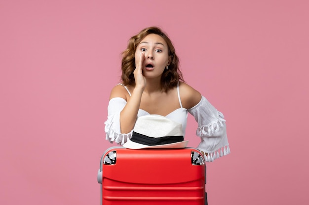 Vue de face d'une jeune femme se préparant pour des vacances avec un sac rouge appelant quelqu'un sur un mur rose