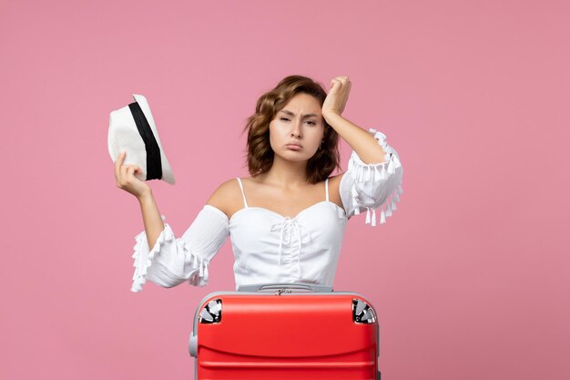 Vue de face d'une jeune femme se préparant pour des vacances avec un sac rouge posant sur le mur rose