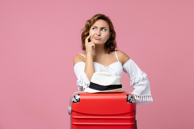 Vue de face d'une jeune femme se préparant pour des vacances avec un sac rouge posant sur le mur rose