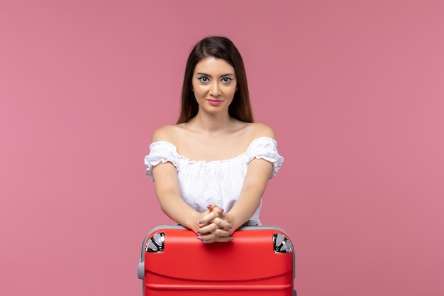 Vue de face jeune femme se préparant pour les vacances avec son sac rouge sur un fond rose voyage voyage en mer femme vacances à l'étranger