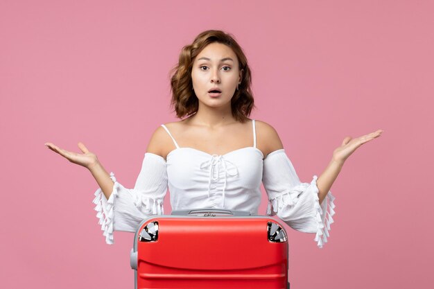 Vue de face d'une jeune femme se préparant pour un voyage d'été avec un sac rouge sur un mur rose