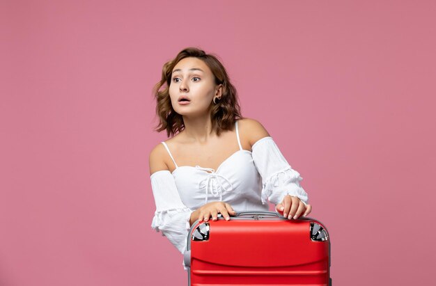 Vue de face d'une jeune femme se préparant pour un voyage avec un sac rouge sur le mur rose