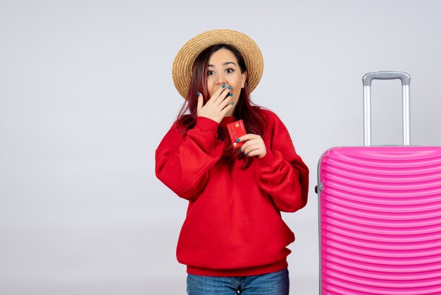 Vue de face jeune femme se préparant pour un voyage et tenant une carte bancaire sur un mur blanc