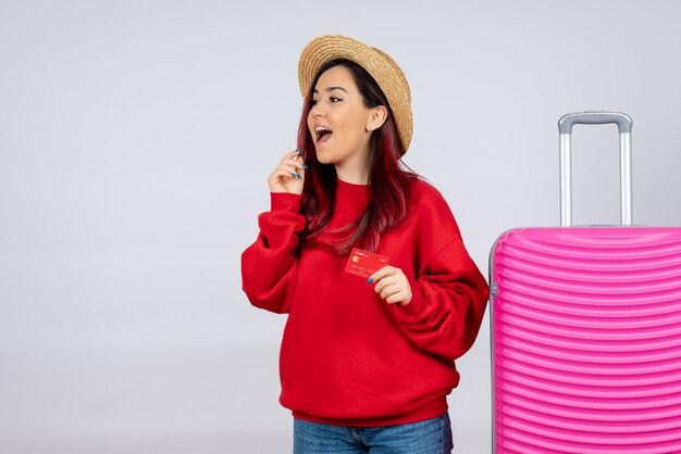 Vue de face jeune femme se préparant pour un voyage et tenant une carte bancaire sur un mur blanc