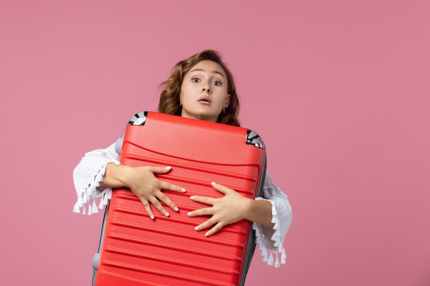 Vue de face d'une jeune femme se préparant pour un voyage et tenant un sac rouge sur un mur rose