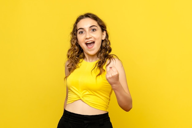 Vue de face de la jeune femme se réjouissant joyeusement sur le mur jaune