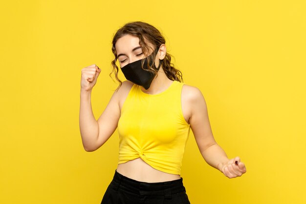 Vue de face de la jeune femme se réjouissant en masque sur mur jaune