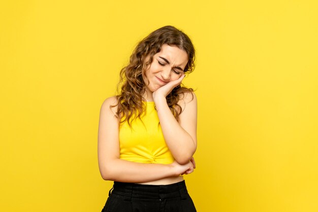 Vue de face de la jeune femme se sentant désolé sur mur jaune