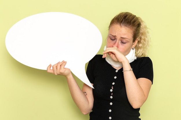 Vue de face jeune femme se sentant très malade et malade tenant un énorme panneau blanc nettoyant son nez sur le mur vert maladie médecine maladie santé