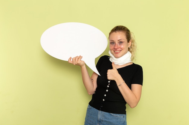 Vue de face jeune femme se sentant très malade et malade tenant un énorme panneau blanc posant et souriant sur le mur vert maladie médecine maladie santé