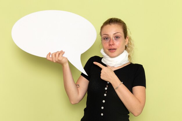 Vue de face jeune femme se sentir très malade et malade tenant un énorme panneau blanc posant sur le mur vert maladie médecine maladie santé