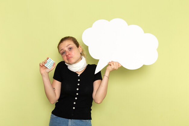 Vue de face jeune femme se sentir très malade et malade tenant un énorme panneau blanc tenant des pilules sur le mur vert clair maladie médecine maladie santé