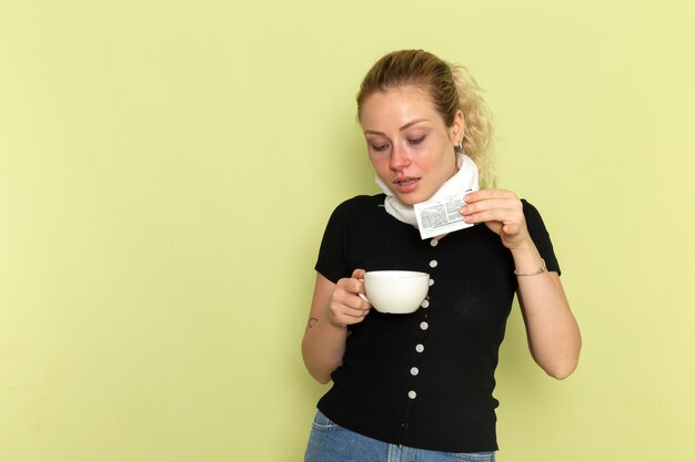 Vue de face jeune femme se sentir très malade et malade tenant une tasse de café et de médicaments sur le mur vert maladie médecine maladie santé