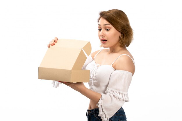 Une vue de face jeune femme séduisante en chemise blanche et jean bleu obtenant petit paquet l'ouvrant sur le blanc