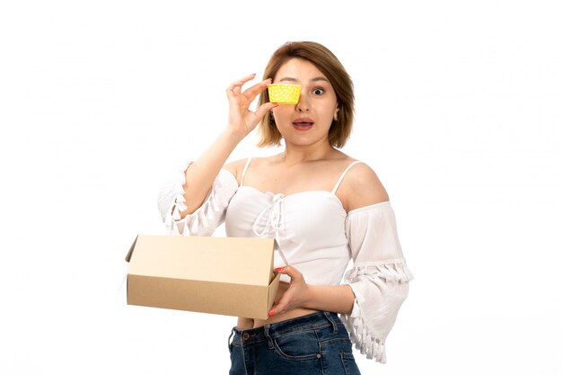Une vue de face jeune femme séduisante en chemise blanche et jean bleu obtenant petit paquet l'ouvrant tenant présent jaune sur le blanc