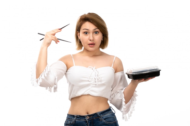 Une vue de face jeune femme séduisante en chemise blanche et jean bleu tenant des bâtons et bol avec repas sur le blanc