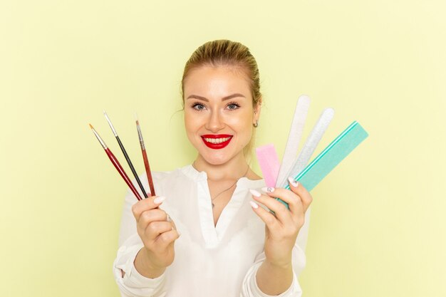 Vue de face jeune femme séduisante en chemise blanche tenant des glands et des accessoires de manucure sur la surface verte