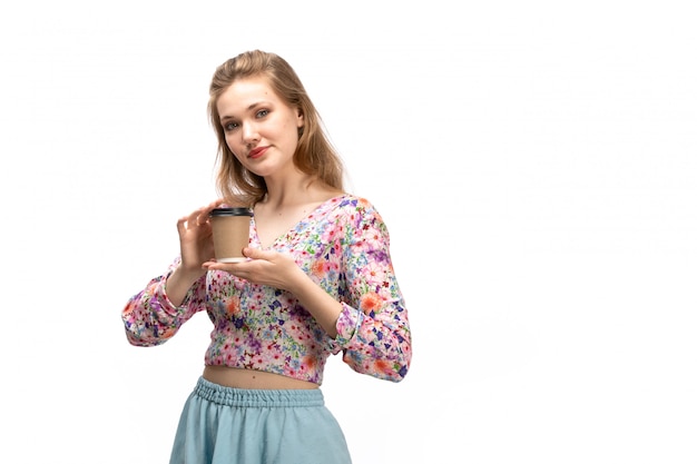 Une vue de face jeune femme séduisante en chemise colorée et jupe bleue tenant une tasse de café sur le blanc