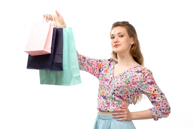 Une vue de face jeune femme séduisante en chemise conçue de fleurs colorées et jupe bleue tenant des paquets commerciaux sur le blanc