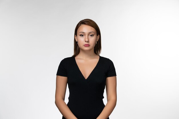 Vue de face jeune femme séduisante en chemise noire juste debout sur une surface blanche