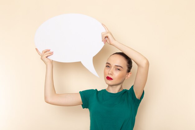 Vue de face jeune femme séduisante en chemise vert foncé et jean bleu tenant une pancarte blanche sur beige