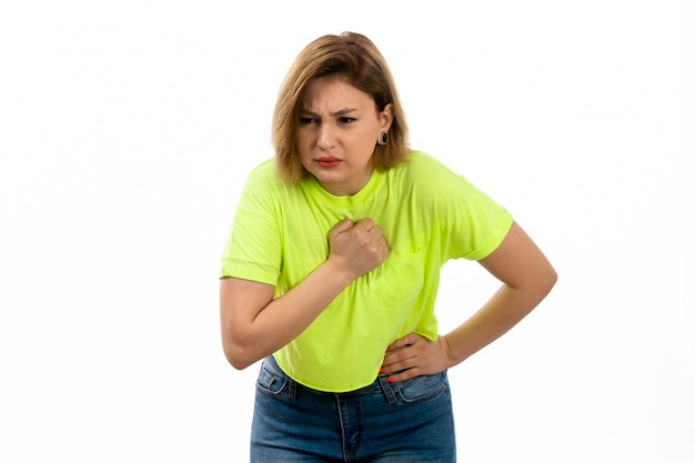 Une vue de face jeune femme séduisante en chemise verte et blue-jeans souffrant de maux d'estomac sur le blanc