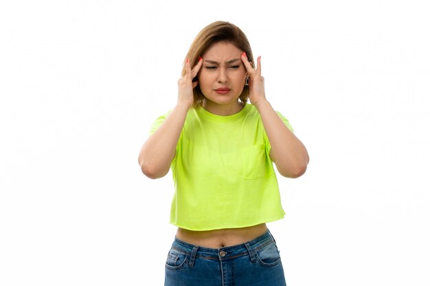 Une vue de face jeune femme séduisante en chemise verte et blue-jeans souffrant de maux de tête sur le blanc