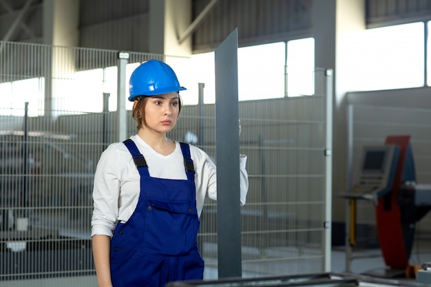 Photo gratuite une vue de face jeune femme séduisante en costume de construction bleu et casque de travail tenant des détails métalliques lourds pendant la construction de l'architecture des bâtiments pendant la journée