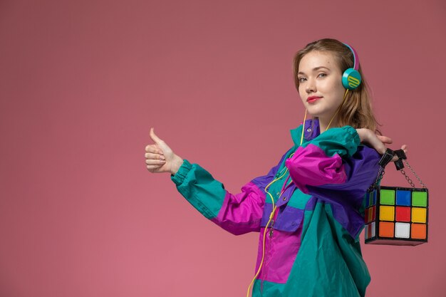 Vue de face jeune femme séduisante en manteau coloré, écouter de la musique sur le mur rose foncé couleur modèle femme jeune fille