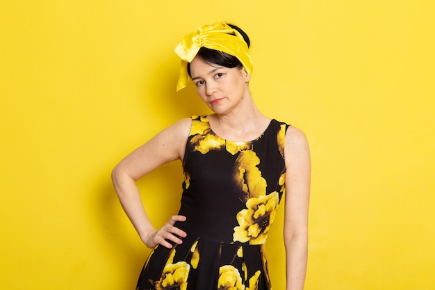 Une vue de face jeune femme séduisante en robe de fleur jaune-noir conçu avec un bandage jaune sur la tête posant sur le jaune