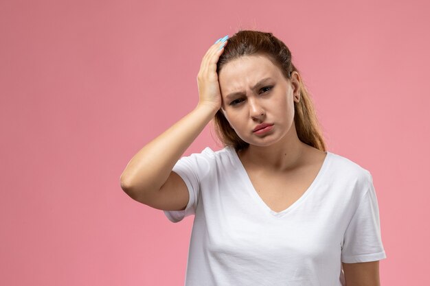 Vue de face jeune femme séduisante en t-shirt blanc ayant un mal de tête sévère sur le fond rose