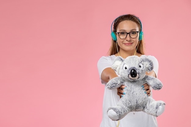 Vue de face jeune femme séduisante en t-shirt blanc, écouter de la musique tenant un jouet sur le fond rose