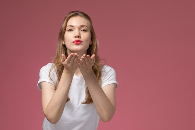 Vue de face jeune femme séduisante en t-shirt blanc envoi de bisous d'air sur un mur rose foncé couleur modèle femme jeune fille