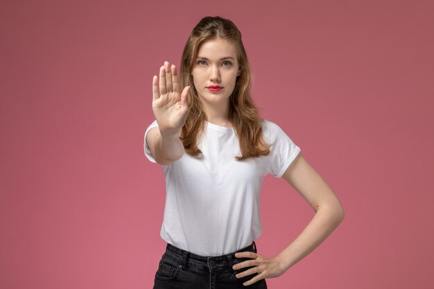 Vue de face jeune femme séduisante en t-shirt blanc et pantalon noir posant panneau d'arrêt showign sur le mur rose modèle femme pose photo couleur