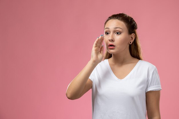 Vue de face jeune femme séduisante en t-shirt blanc posant essayant d'appeler sur le fond rose