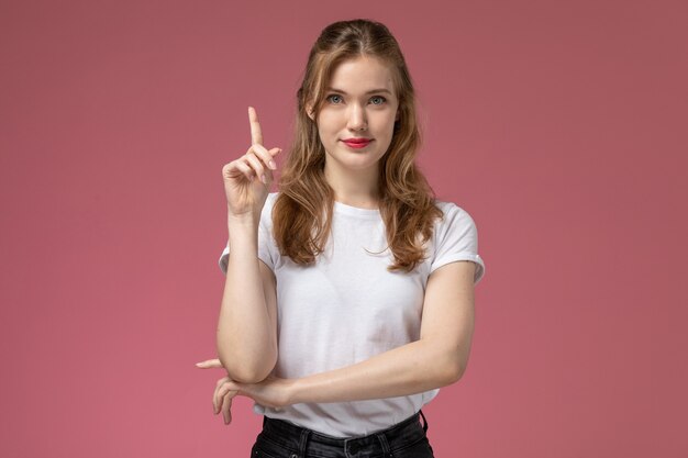 Vue de face jeune femme séduisante en t-shirt blanc posant avec une expression ravie sur le mur rose modèle femme pose couleur jeune femme