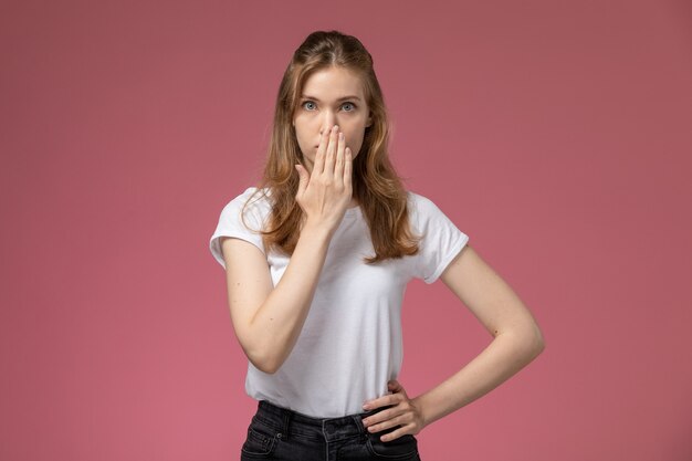 Vue de face jeune femme séduisante en t-shirt blanc posant avec une expression de surprise sur le mur rose foncé couleur modèle femme jeune fille