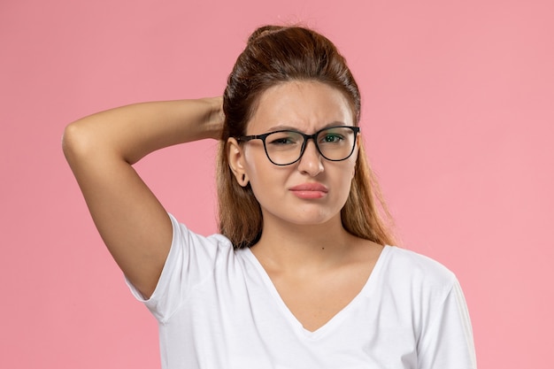 Photo gratuite vue de face jeune femme séduisante en t-shirt blanc posant juste et ayant mal à la tête sur le fond rose