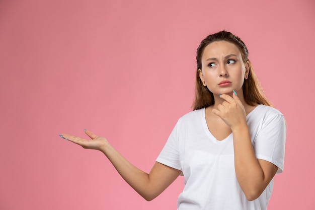 Vue de face jeune femme séduisante en t-shirt blanc posant et pensant sur le fond rose