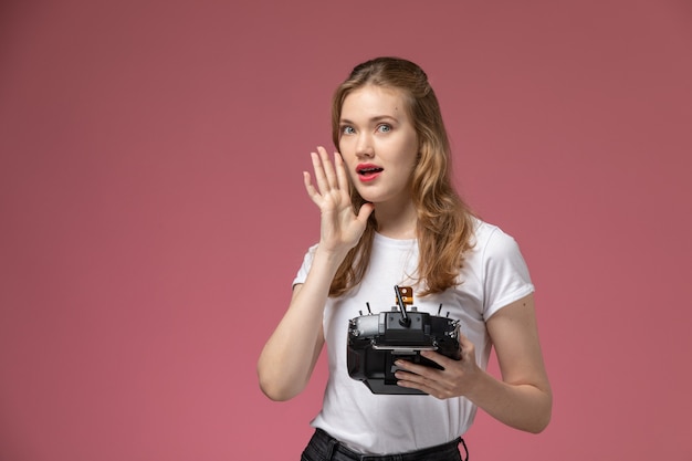 Vue de face jeune femme séduisante en t-shirt blanc posant avec télécommande sur mur rose modèle couleur femme jeune fille