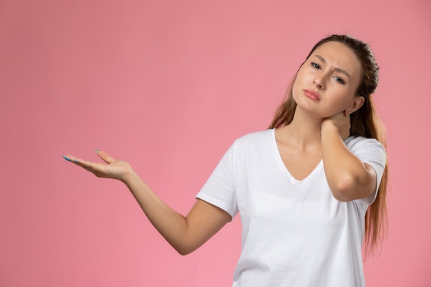 Vue de face jeune femme séduisante en t-shirt blanc souffrant de maux de cou sur fond rose