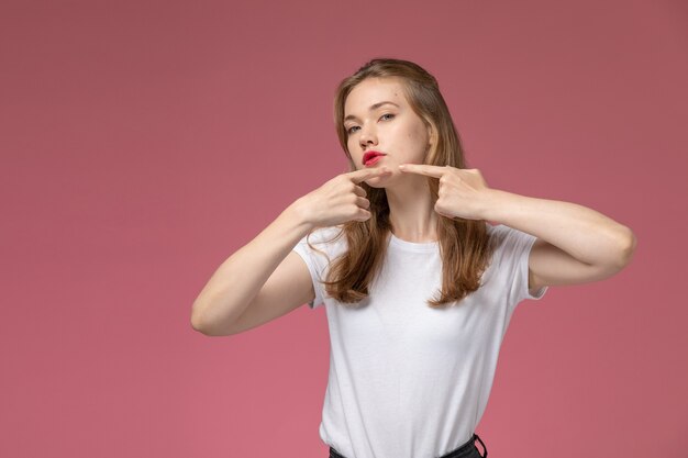 Vue de face jeune femme séduisante en t-shirt blanc touchant son acné sur le mur rose foncé couleur modèle femme jeune fille