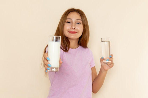 Vue de face jeune femme séduisante en t-shirt rose et blue-jeans tenant du lait et de l'eau avec sourire