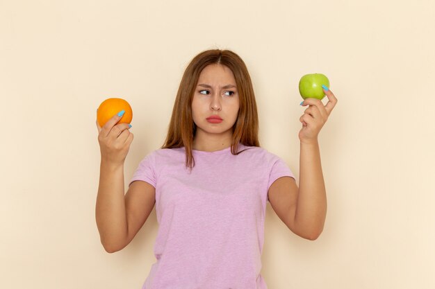 Vue de face jeune femme séduisante en t-shirt rose et blue-jeans tenant orange et apple