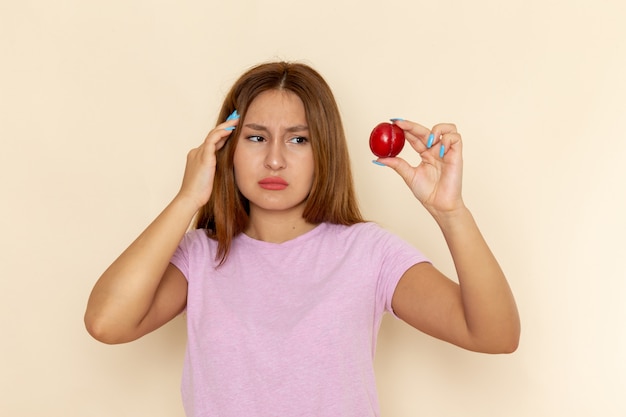 Vue de face jeune femme séduisante en t-shirt rose et blue-jeans tenant prune aigre fraîche