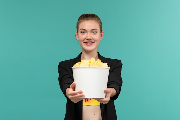 Vue de face jeune femme séduisante tenant cips et regarder un film sur la surface bleu clair