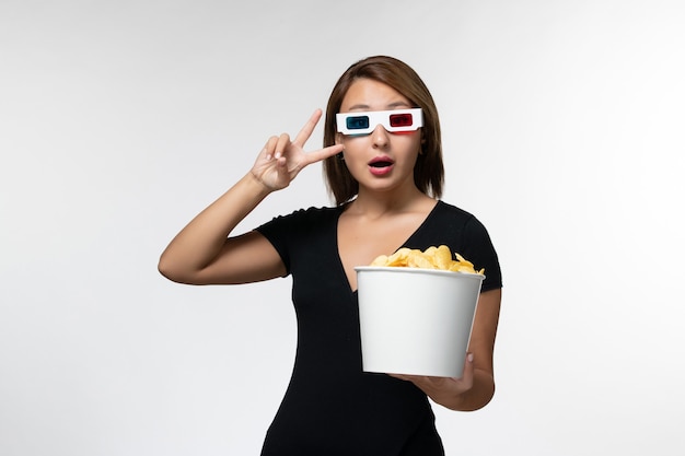 Vue de face jeune femme séduisante tenant le panier avec des cips de pommes de terre dans des lunettes de soleil sur une surface blanche