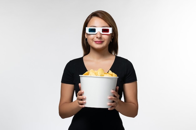 Vue de face jeune femme séduisante tenant le panier avec des cips de pommes de terre dans des lunettes de soleil sur une surface blanche