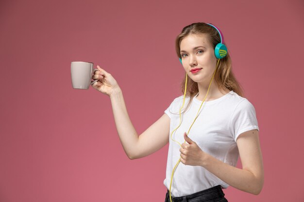 Vue de face jeune femme séduisante tenant tasse et écouter de la musique sur le mur rose modèle couleur femme jeune fille