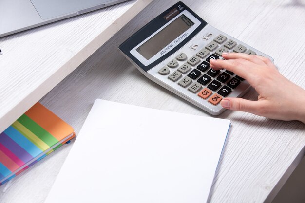 Une vue de face jeune femme séduisante travaillant avec des documents en face de la table avec des calculatrices tasse téléphone fond clair travailler les technologies de l'entreprise